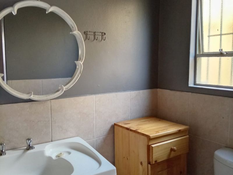 A functional bathroom featuring a vanity basin, tiled splashback, and a window with security bars.