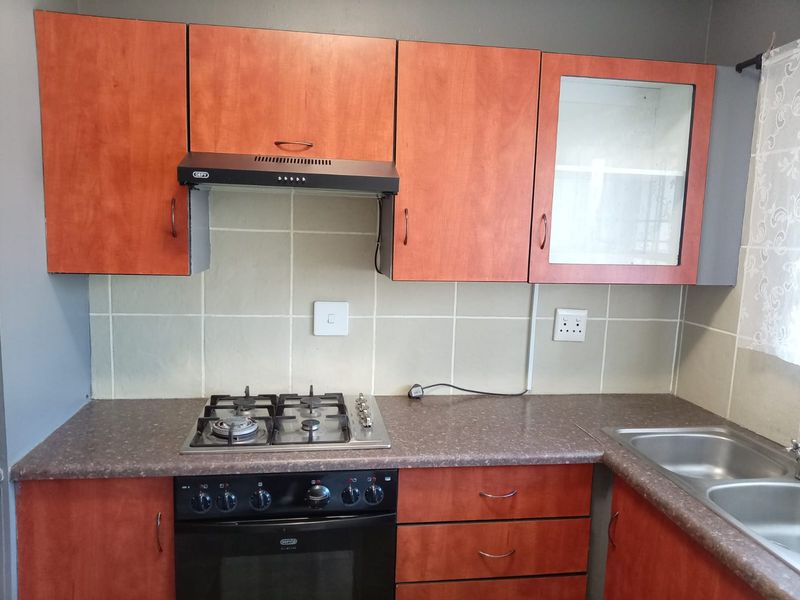 A functional kitchen featuring wood-look cabinetry, a gas hob with extractor fan, built-in oven, and a double stainless steel sink with tiled backsplash.