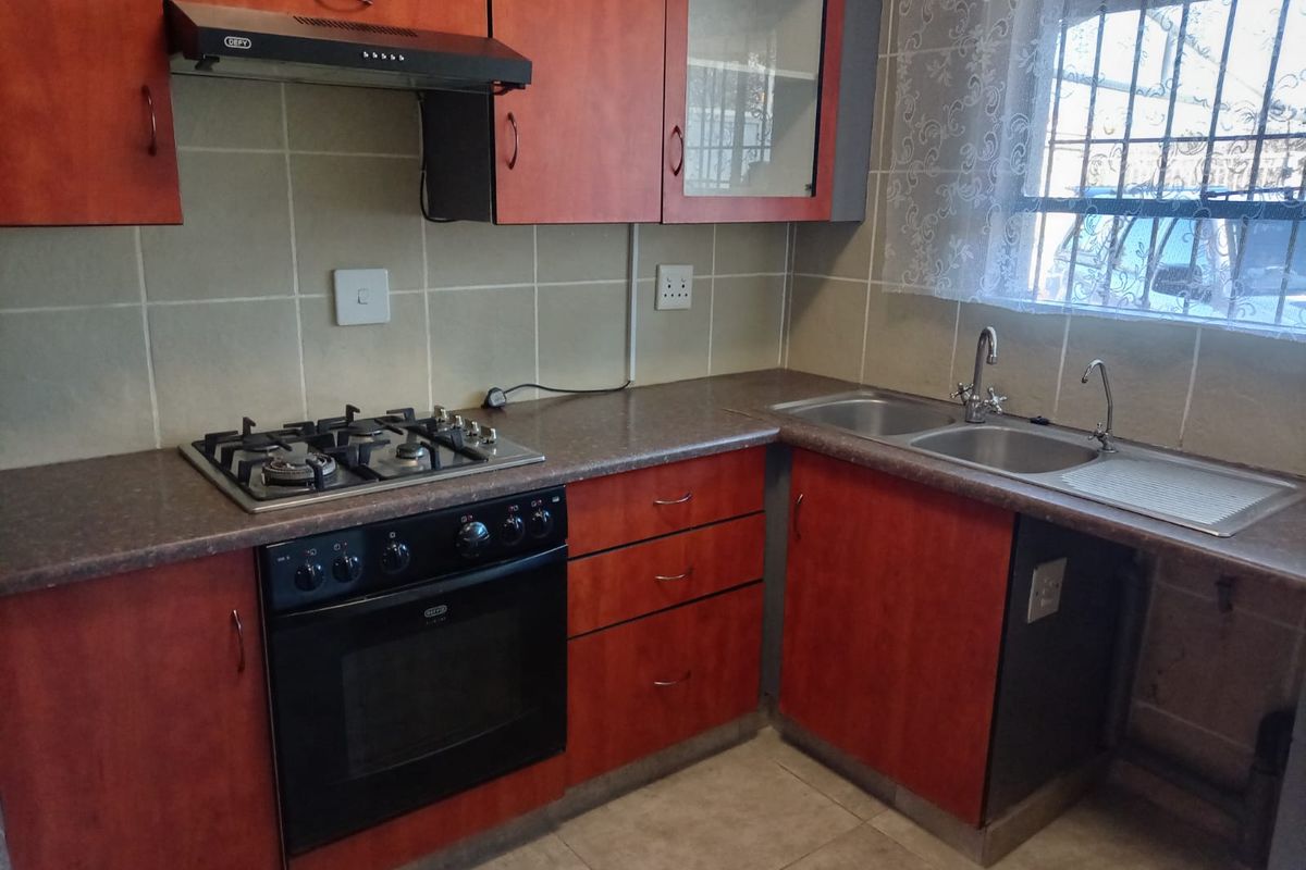 A functional kitchen featuring wood-look cabinetry, laminate countertops, a gas hob with extractor, and a double stainless steel sink with tiled splashbacks.