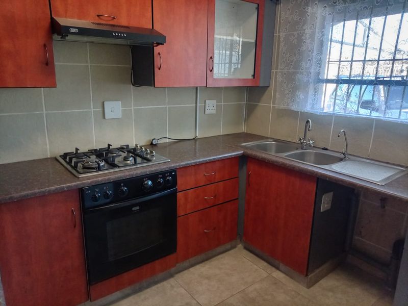 A functional kitchen featuring wood-look cabinetry, laminate countertops, a gas hob with extractor, and a double stainless steel sink with tiled splashbacks.
