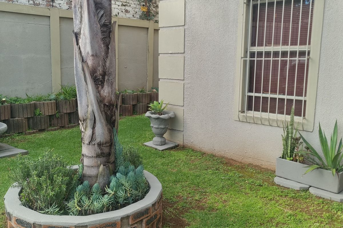 A rear garden area featuring a brick planter, lawn, and a building facade with security bars on the window.