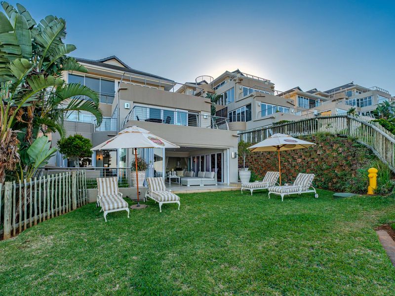 Rear view of a multi-level residential property featuring a landscaped garden, lawn area, and spacious terrace with glass sliding doors.