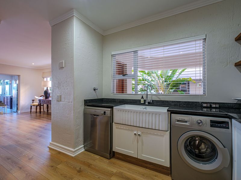A well-appointed scullery featuring a farmhouse sink, granite countertops, and integrated laundry appliances, seamlessly connected to the main living area.