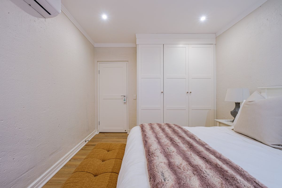 A well-maintained bedroom featuring built-in cupboards, recessed downlighting, and a split-system air conditioning unit.