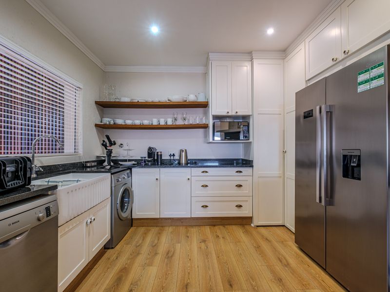 A well-appointed scullery featuring farmhouse sink, granite countertops, shaker cabinetry, and open timber shelving, providing efficient additional kitchen workspace.