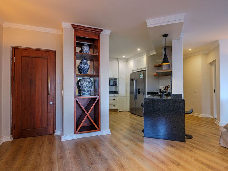 Open plan kitchen area featuring a granite island, built-in wooden shelving, and modern laminate flooring with recessed and pendant lighting.