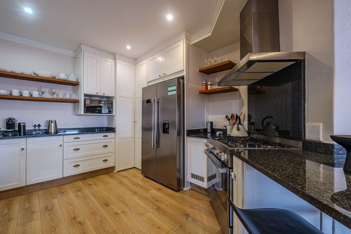 Modern kitchen featuring white shaker-style cabinetry, granite countertops, high-end stainless steel appliances, and warm timber shelving with recessed lighting.
