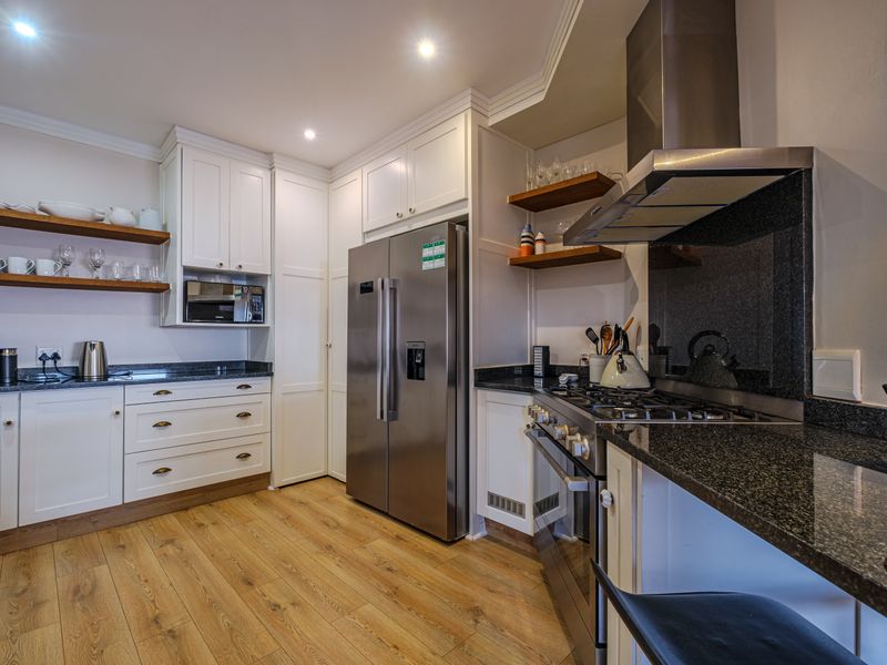 Modern kitchen featuring white shaker-style cabinetry, granite countertops, high-end stainless steel appliances, and warm timber shelving with recessed lighting.