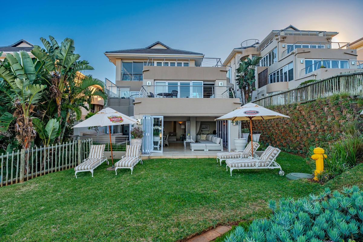 Rear view of the property featuring a landscaped garden, tiled patio area, and a balcony with stainless steel balustrades overlooking the lawn.