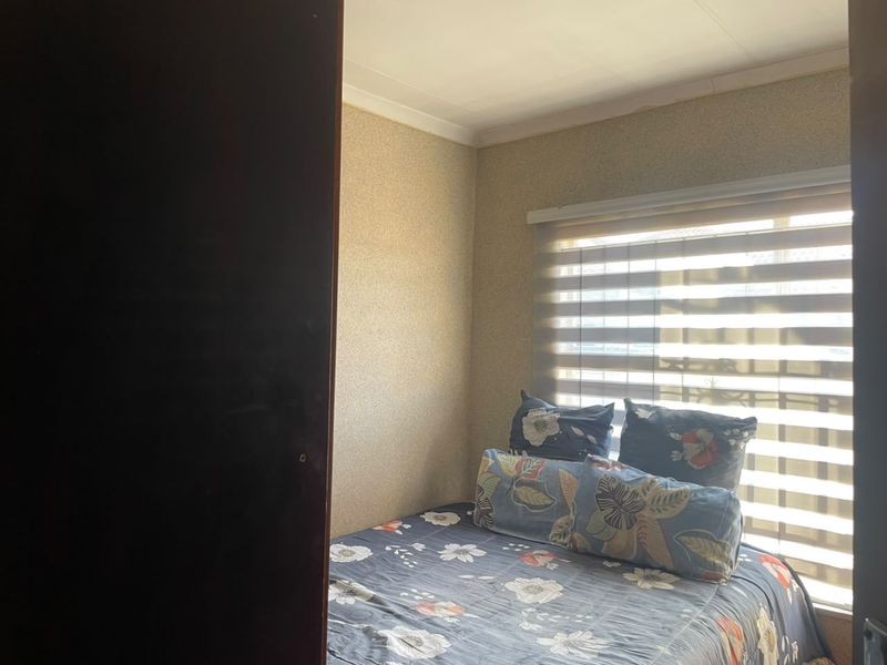 A compact bedroom featuring textured wallpaper, coving, and a window fitted with modern roller blinds.