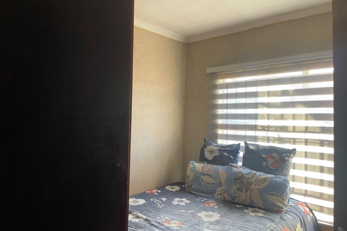 A compact bedroom featuring textured wallpaper, coving, and a window fitted with modern roller blinds.