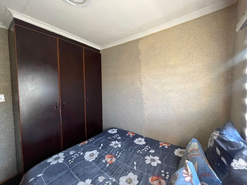 A bedroom featuring a built-in wardrobe and textured wall finishes, currently showing signs of moisture damage on the wall surface.