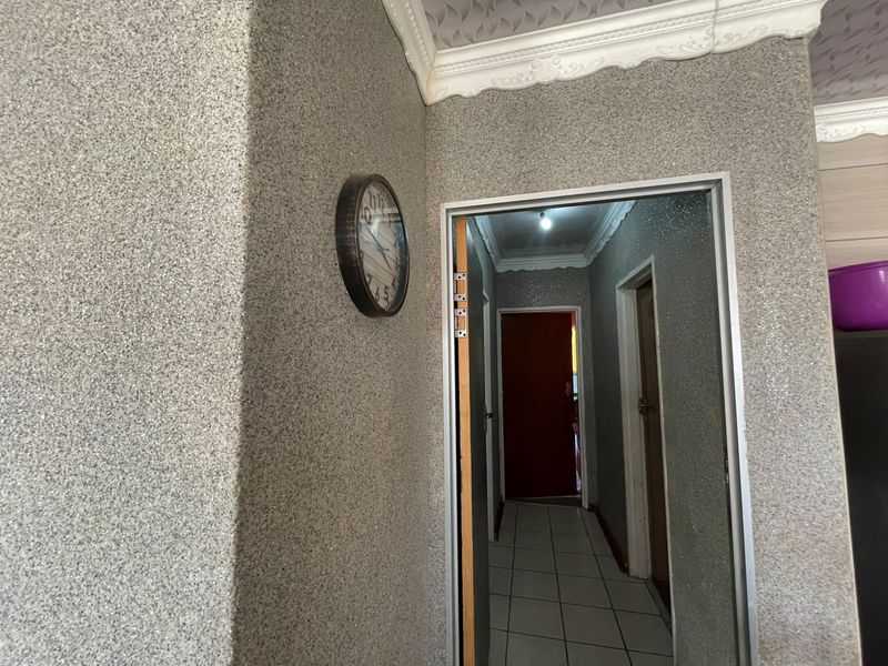 A hallway featuring textured wall finishes, decorative cornicing, and tiled flooring, providing access to adjacent rooms.