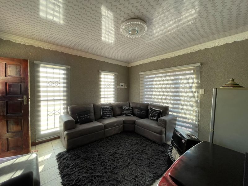A living room featuring textured wallpaper, decorative ceiling molding, patterned ceiling tiles, tiled flooring, and window security bars with roller blinds.