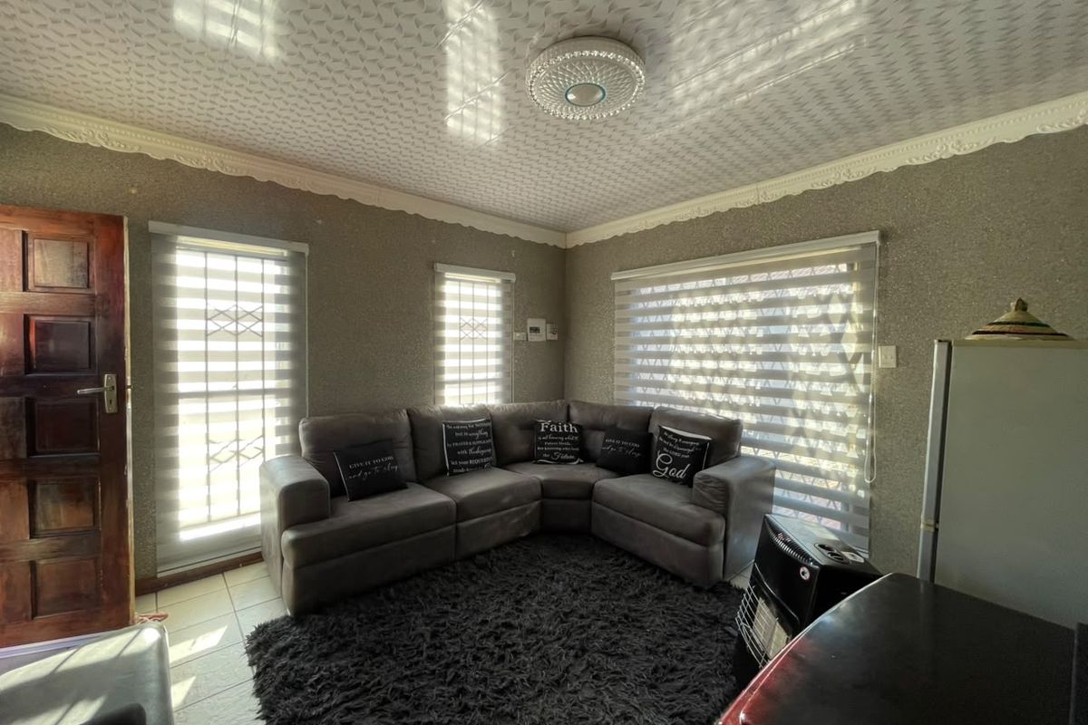 A living room featuring textured wallpaper, decorative ceiling molding, patterned ceiling tiles, tiled flooring, and window security bars with roller blinds.