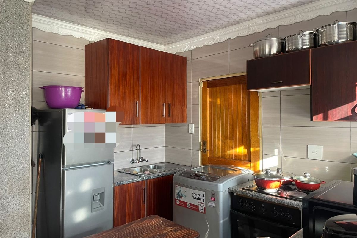 A functional kitchen featuring wood-finish cabinetry, tiled walls, a stainless steel sink, and a freestanding stove with integrated extractor fan.