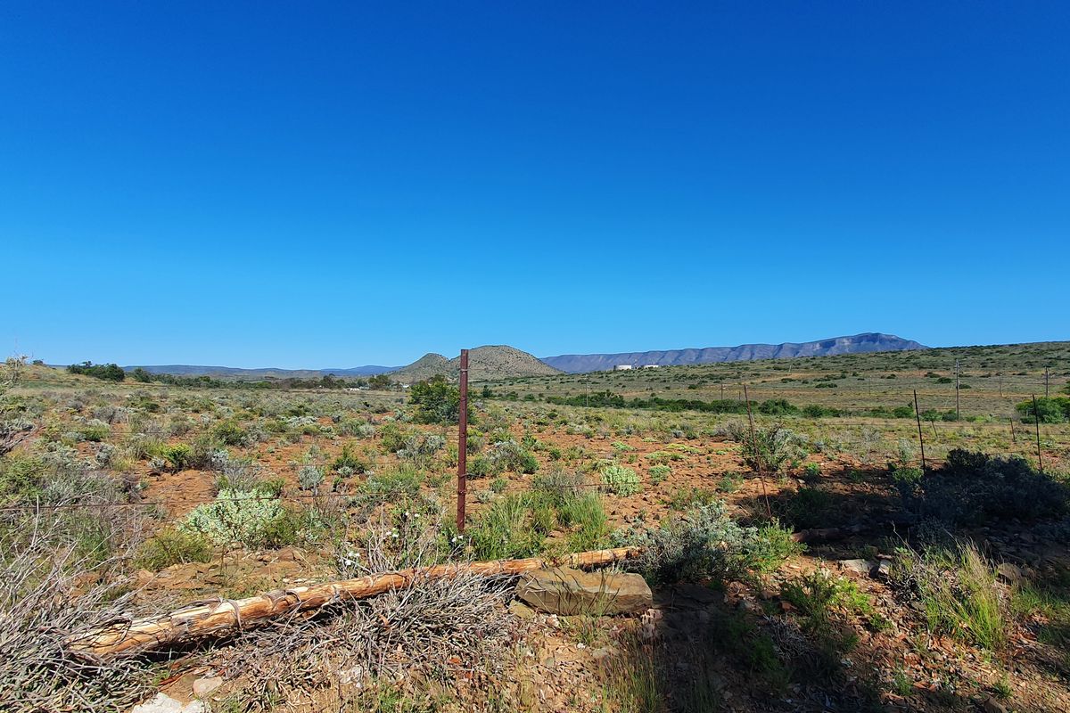 A wide-angle view of vacant residential land featuring natural scrub vegetation, wire fencing, and distant mountain range vistas.