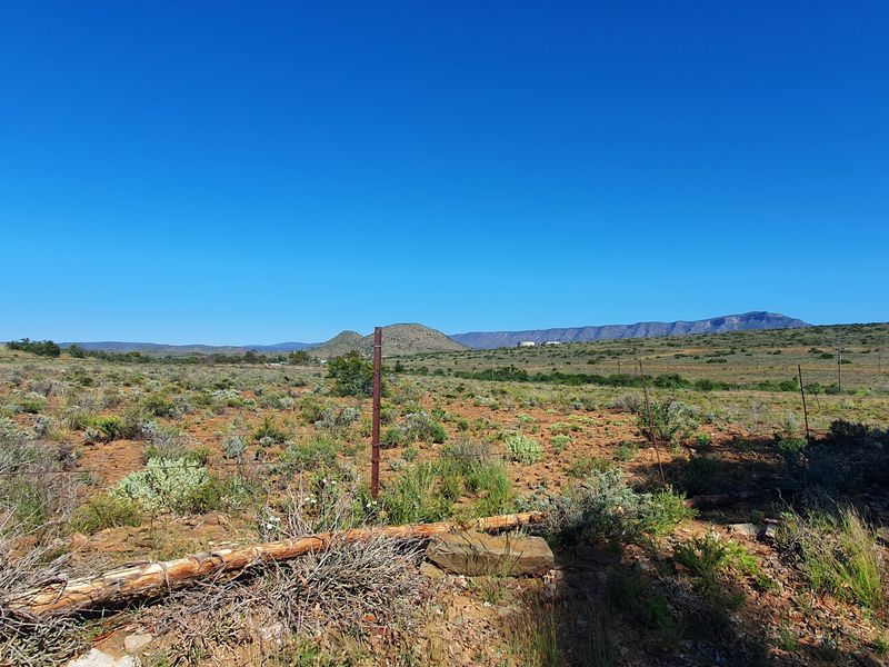 A wide-angle view of vacant residential land featuring natural scrub vegetation, wire fencing, and distant mountain range vistas.