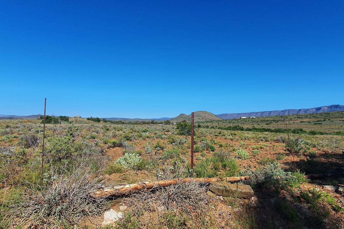 A wide-angle view of vacant residential land featuring natural scrub vegetation, distant mountain ranges, and perimeter wire fencing.