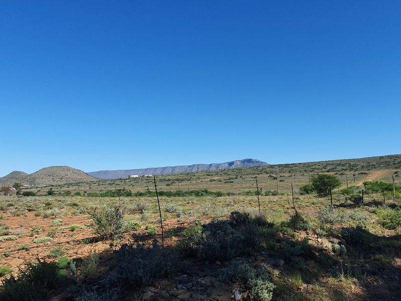 A wide-angle view of the vacant residential land featuring natural landscape, native vegetation, and distant mountain ranges.