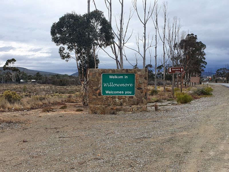 A view of the roadside entrance signage welcoming visitors to Willowmore, featuring a stone-clad sign structure and surrounding rural landscape.