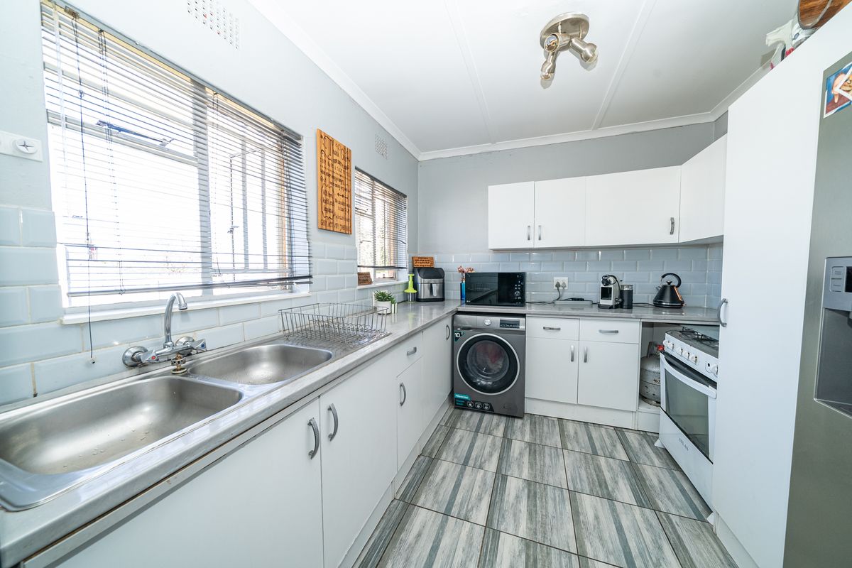 Functional kitchen featuring white cabinetry, subway tile backsplash, double basin sink, and integrated laundry space with gas stove and oven.