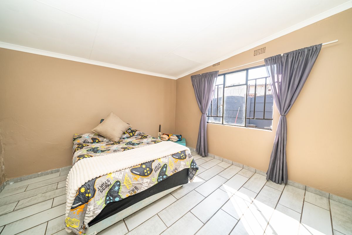 A bedroom featuring tiled flooring, a metal-framed window with security bars, and neutral wall paint.