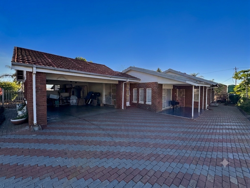 Front view of a brick house featuring a spacious paved driveway, a covered carport, and an attached covered patio area.