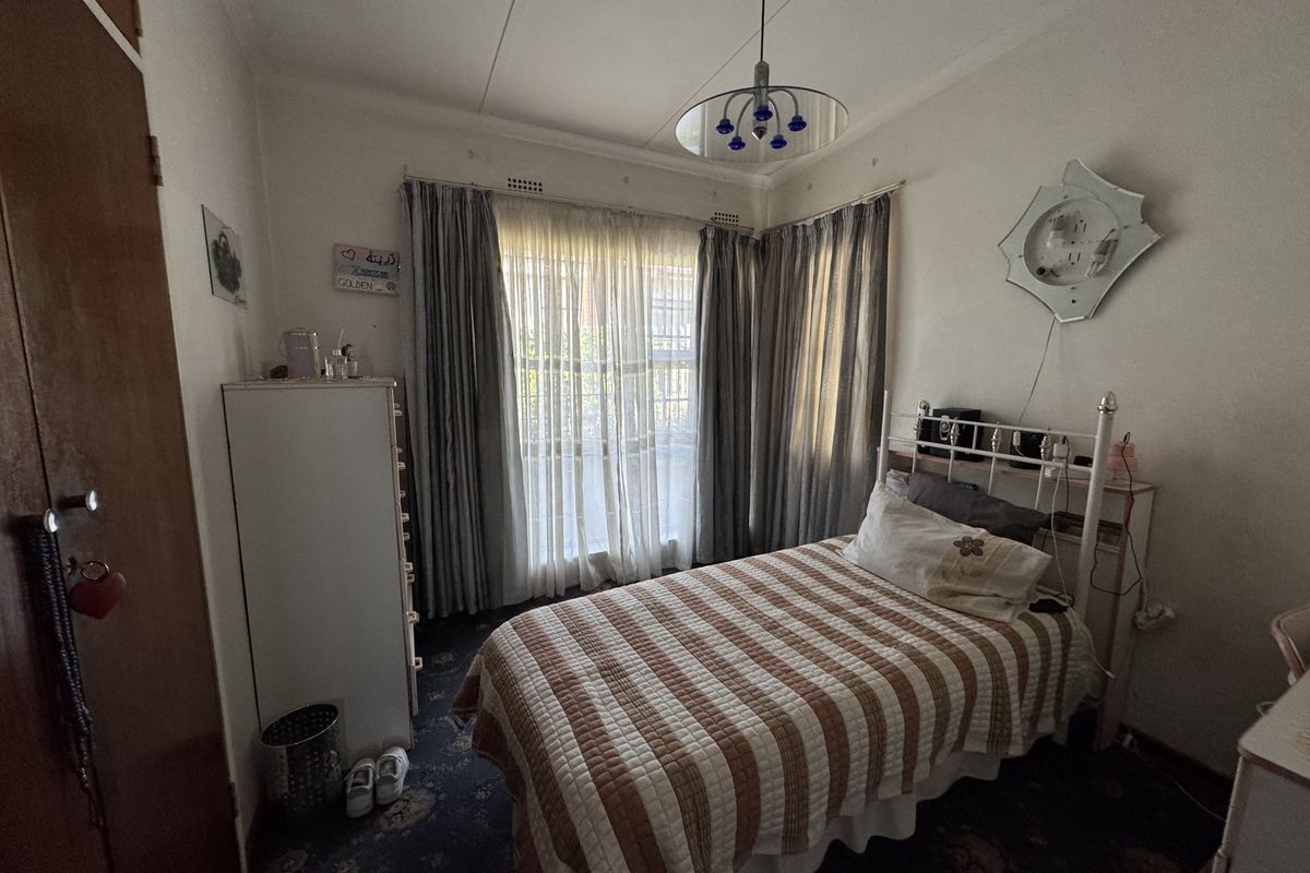 A compact bedroom featuring a built-in wardrobe, large window with curtain tracks, and dated carpet flooring, offering potential for modernization.