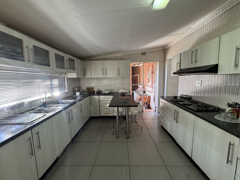A functional kitchen featuring extensive built-in cabinetry, laminate countertops, a double basin sink, and an integrated electric hob with an extractor fan.
