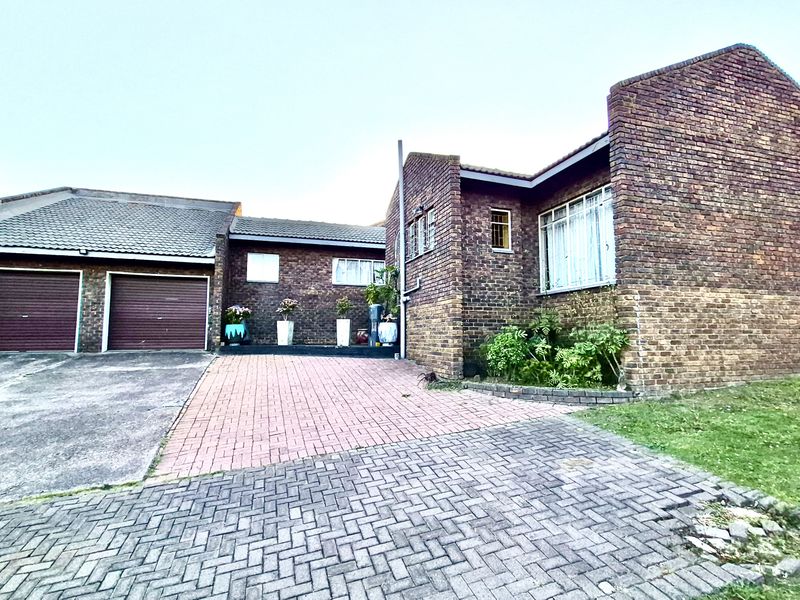 Front exterior view of a brick house featuring a double garage, paved driveway, and established garden area.