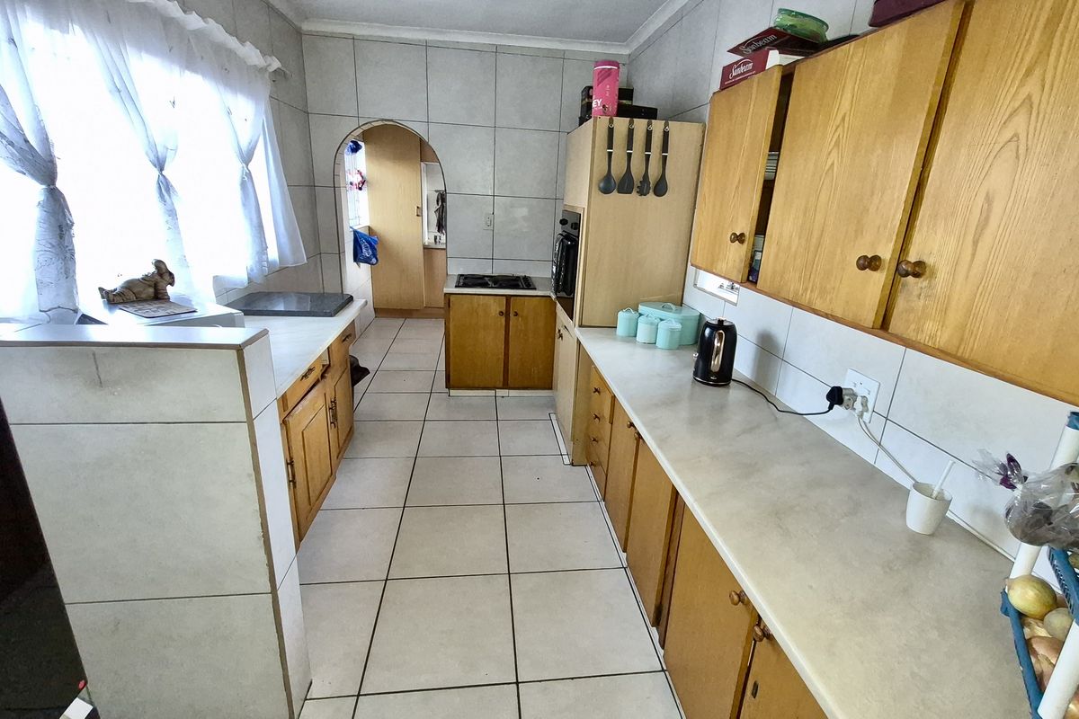 A functional galley-style kitchen featuring wooden cabinetry, tiled surfaces, and a built-in oven, offering potential for a modern renovation.