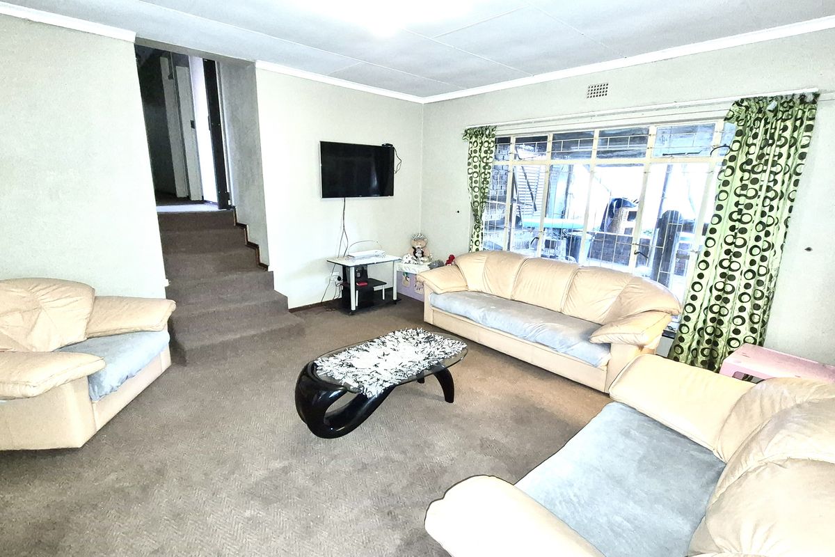 A living room featuring carpeted flooring, steel-framed windows, and an internal staircase leading to an upper level.