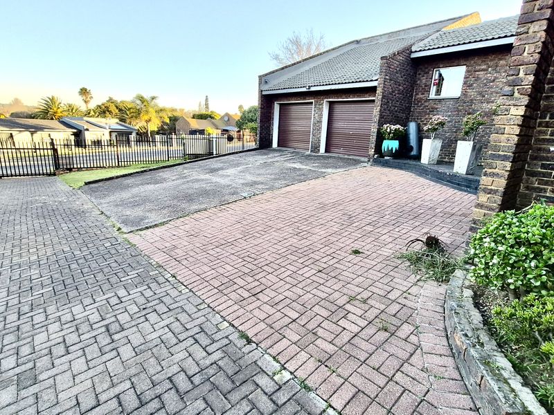 Front exterior view of a facebrick house featuring a double garage, paved driveway, and secure perimeter fencing.