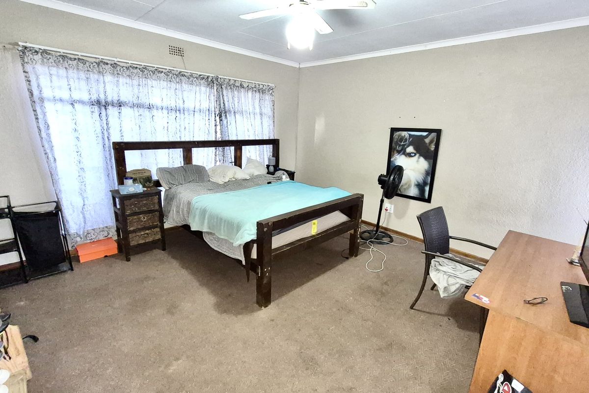 A spacious bedroom featuring carpeted flooring, a ceiling fan, and large windows with curtain rails, offering a blank canvas for potential updates.
