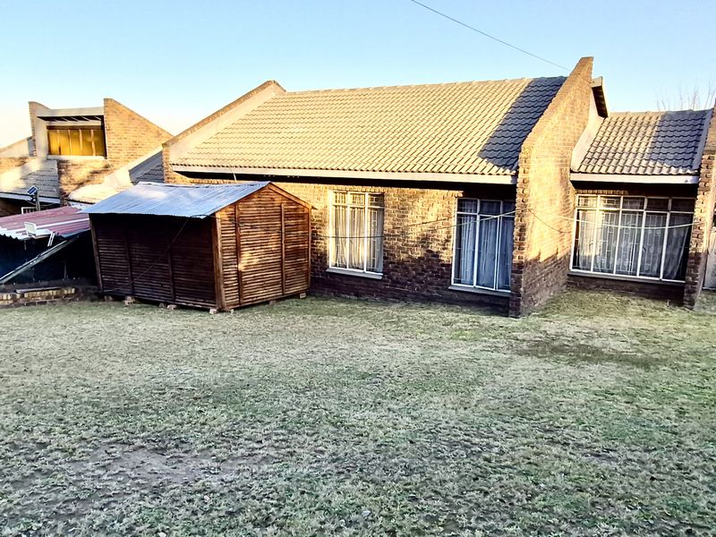 Rear view of a brick house featuring a tiled roof, aluminium windows, and a detached timber garden shed set within a spacious lawn area.