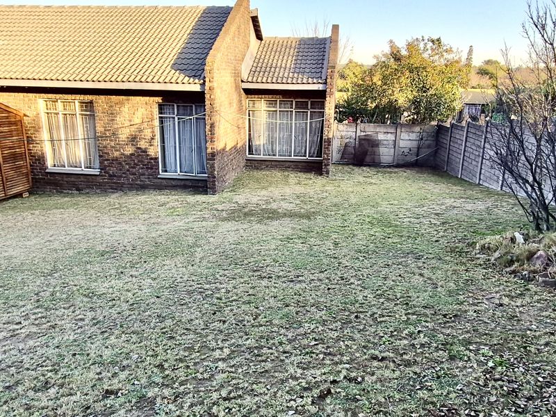 Rear view of a face brick house featuring a tiled roof, a private garden, and a precast concrete boundary wall.