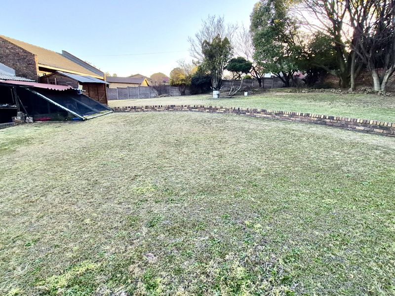 A spacious backyard featuring a large lawn area, a low brick retaining wall, and established perimeter boundary walls.