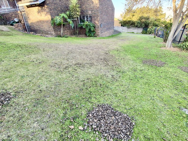 A view of the rear garden area featuring a face brick building facade, metal perimeter fencing, and an established lawn.