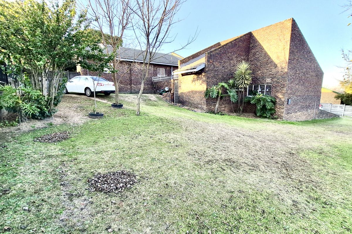 A view of the rear exterior of the house featuring a face brick facade, tiled roof, and a large grassed garden area.