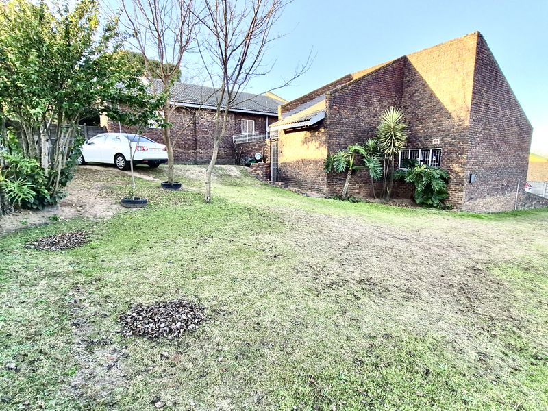 A view of the rear exterior of the house featuring a face brick facade, tiled roof, and a large grassed garden area.