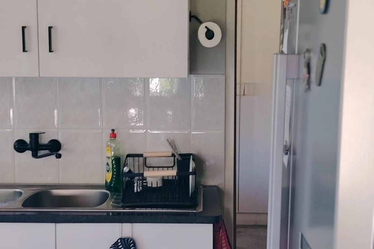 A functional kitchen area featuring white cabinetry, a stainless steel sink with a modern black tap, and a tiled splashback.