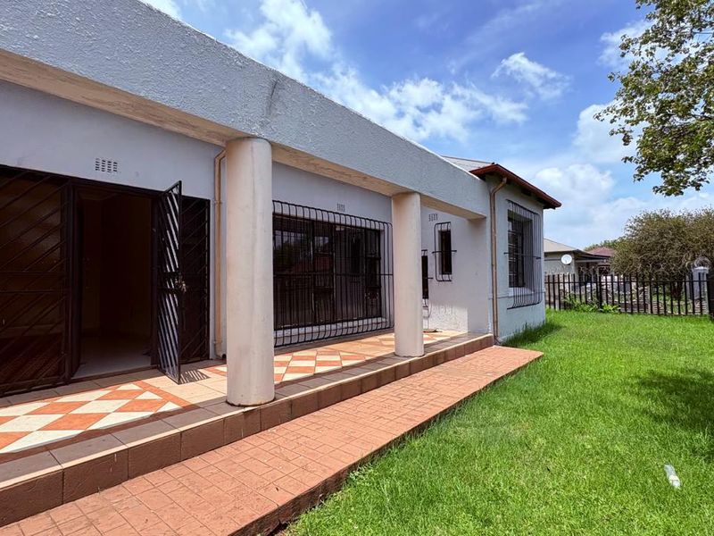 A covered patio area featuring tiled flooring and concrete columns, overlooking a private garden with perimeter security fencing.