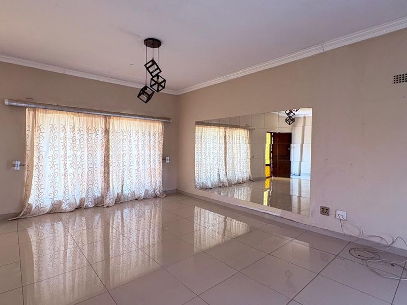 Spacious living area featuring polished tile flooring, decorative cove cornicing, a large wall-mounted mirror, and a modern pendant light fixture.