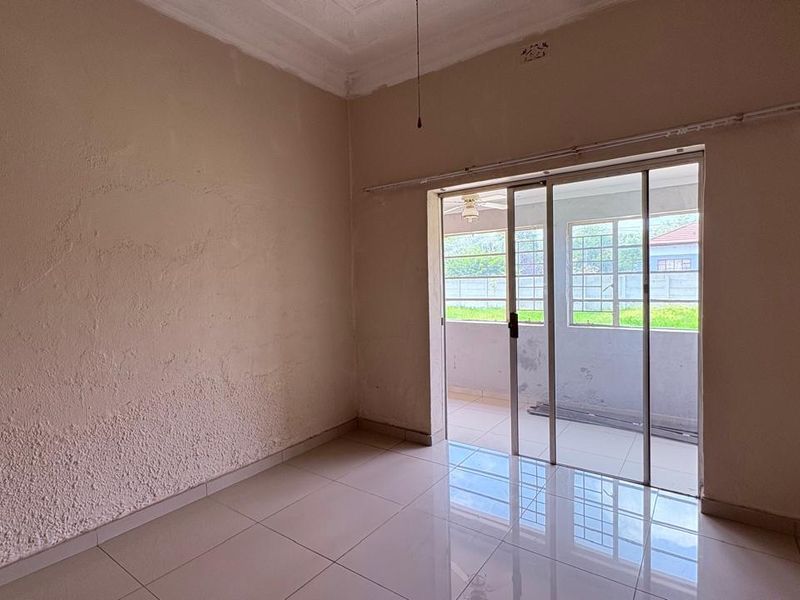 An empty living room featuring tiled flooring and a sliding glass door leading to an outdoor patio area.