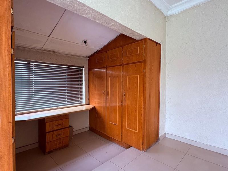 A bedroom featuring built-in wooden cupboards, a matching built-in desk, tiled flooring, and venetian blinds.
