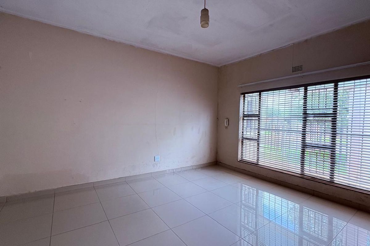 An empty living room featuring tiled flooring and large windows with venetian blinds, requiring minor cosmetic updates to the walls and ceiling.