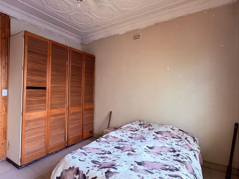 A bedroom featuring a built-in wooden wardrobe, decorative pressed metal ceiling, tiled flooring, and window security bars.