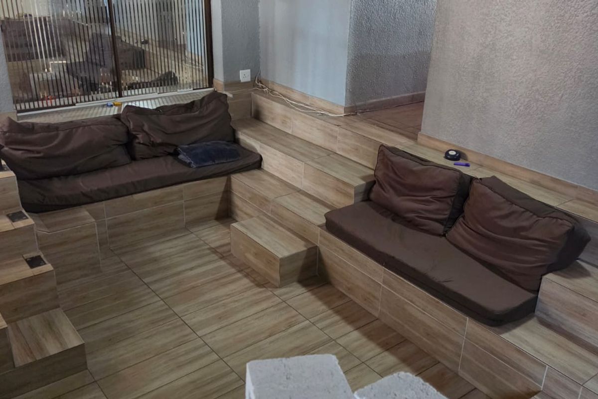 A sunken living area featuring built-in tiled seating platforms and tiled flooring, requiring cosmetic updates to improve the overall aesthetic.