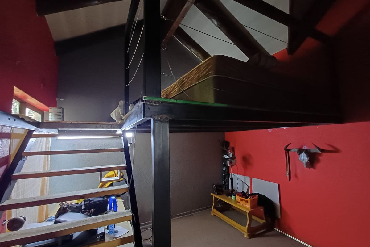 A bedroom featuring a mezzanine loft level with exposed timber roof trusses and a steel staircase structure.